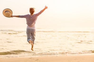 une femme qui court vers la mer avec son chapeau