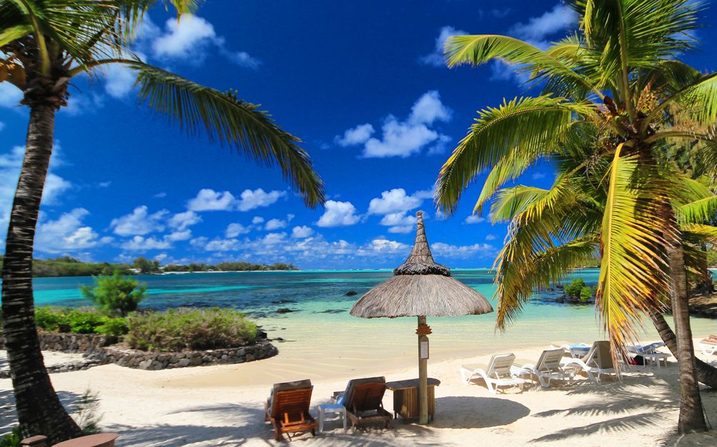 Plage de sable blanc à l'île Maurice avec une eau turquoise, des palmiers, un parasol et plusieurs chaises longues